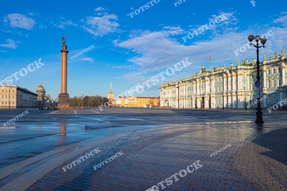 На фотографии запечатлена Дворцовая площадь Санкт-Петербурга, освещённая утренним солнцем. В центре площади возвышается Александровская колонна, символизирующая победу России в Отечественной войне 1812 года. Справа виден Зимний дворец, выполненный в стиле елизаветинского барокко. Вдали можно заметить шпиль Адмиралтейства и купол Исаакиевского собора. Пустая площадь создаёт ощущение тишины и величия.